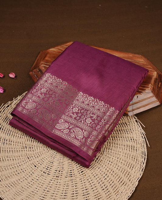 Burgundy colour semi Tussar silk saree featuring an elegant plain body, complemented by a self colour border adorned with traditional gold zari floral kodi patterns. Comes paired with a matching blouse piece.