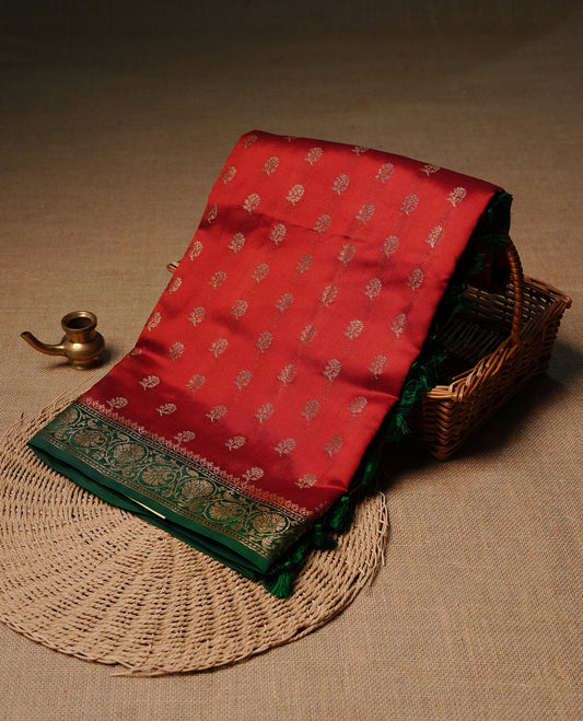 Red colour pure tussar Banaras silk saree featuring intricate gold zari motifs across the body, enhanced with a contrast green floral kodi zari border for a rich traditional look. Comes with a matching blouse piece.
