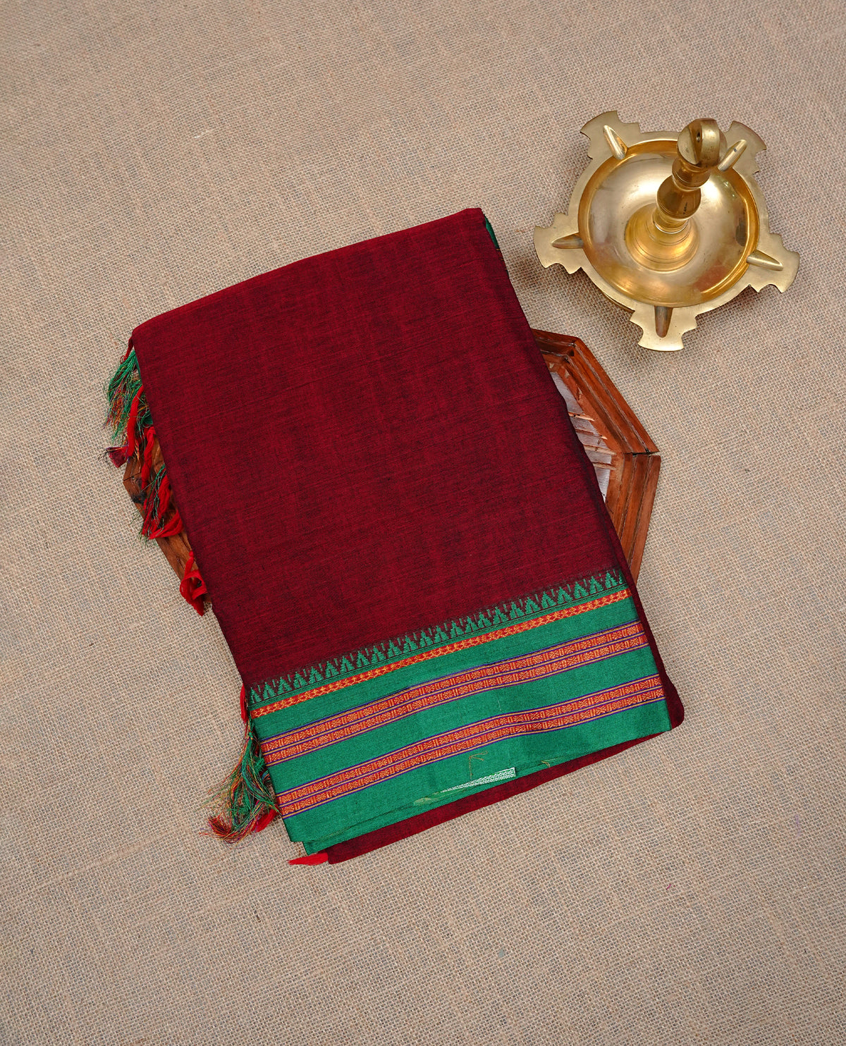 Maroon colour Narayanapattu cotton saree with a plain body, complemented by a Green colour with Gold Zari border & contrast pallu, paired with a matching blouse piece.