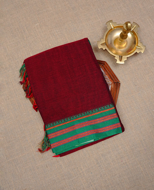Maroon colour Narayanapattu cotton saree with a plain body, complemented by a Green colour with Gold Zari border & contrast pallu, paired with a matching blouse piece.