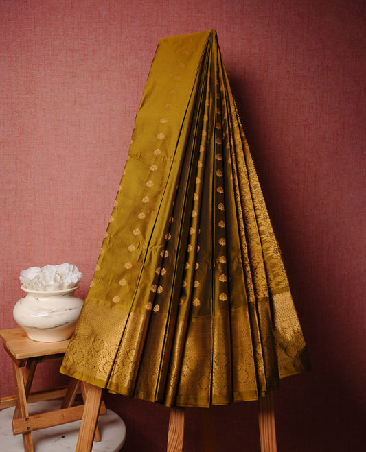Olive colour soft silk saree featuring gold zari motifs on body, complemented by self colour with zari border, paired with matching blouse piece.