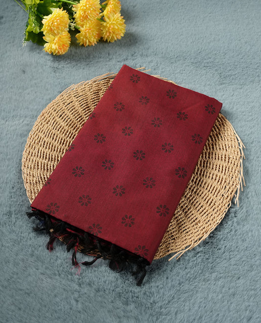 Deep maroon colour poly cotton saree with black floral butti motifs on the body, paired with a matching pallu featuring black ornate floral jaal and stripes on the border, and a coordinated all‑over black paisley printed blouse piece.