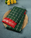 Bottle green colour chettinad cotton saree with silver zari checkered pattern on the body, paired with a contrast red colour pallu featuring silver zari floral border, and a coordinated red checkered blouse piece with matching silver zari border.