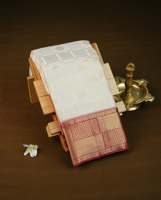 Cream colour semi wedding saree featuring light gold zari box with check with chakra across the body, complemented by maroon colour with  traditional border. Comes with a matching blouse piece.