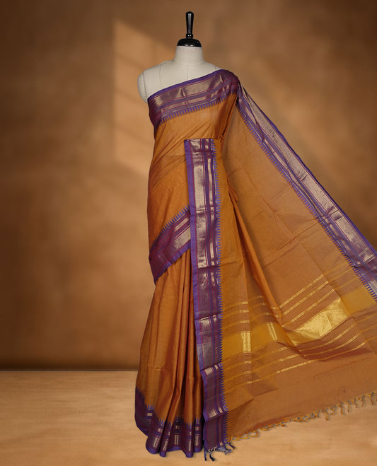 Brown colour chettinad cotton saree featuring elegant plain body highlighting contrast indigo colour with gold zari traditional border, pallu and paired with matching blouse piece.