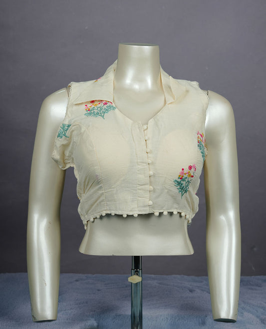 Ivory colour sleeveless cotton blouse with delicate floral embroidery, collared neckline, front button closure, and subtle pom-pom hem detailing for a soft ethnic touch.