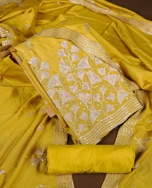warm olive colour churidar material with subtle mirror and thread embroidery, finished with delicate border detailing and paired with a matching plain bottom and dupatta.