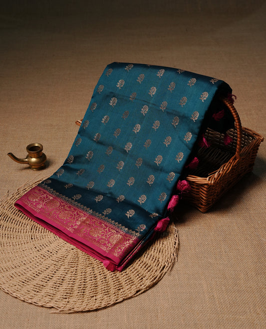 Teal colour pure tussar Banaras silk saree featuring intricate gold zari motifs across the body, enhanced with a contrast Magenta floral kodi zari border for a rich traditional look. Comes with a matching blouse piece.
