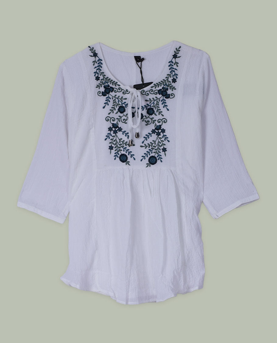 White three-quarter sleeve tunic top with round neckline and front yoke featuring teal and green floral embroidery with tie-up detail at the neck.