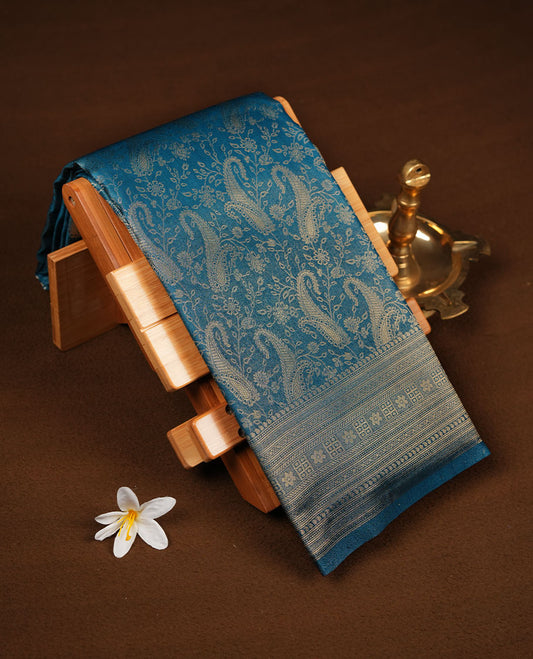 Peacock blue colour semi soft silk brocade saree  featuring elegant gold zari floral and paisley motifs across the body, finished with a richly woven self-colour border and pallu, paired with a matching blouse.