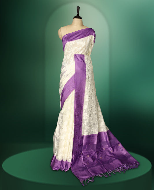 White colour saree adorned with delicate self woven motifs across the body, highlighted with a striking Purple woven border and pallu, finished with tassels, and paired with a matching blouse