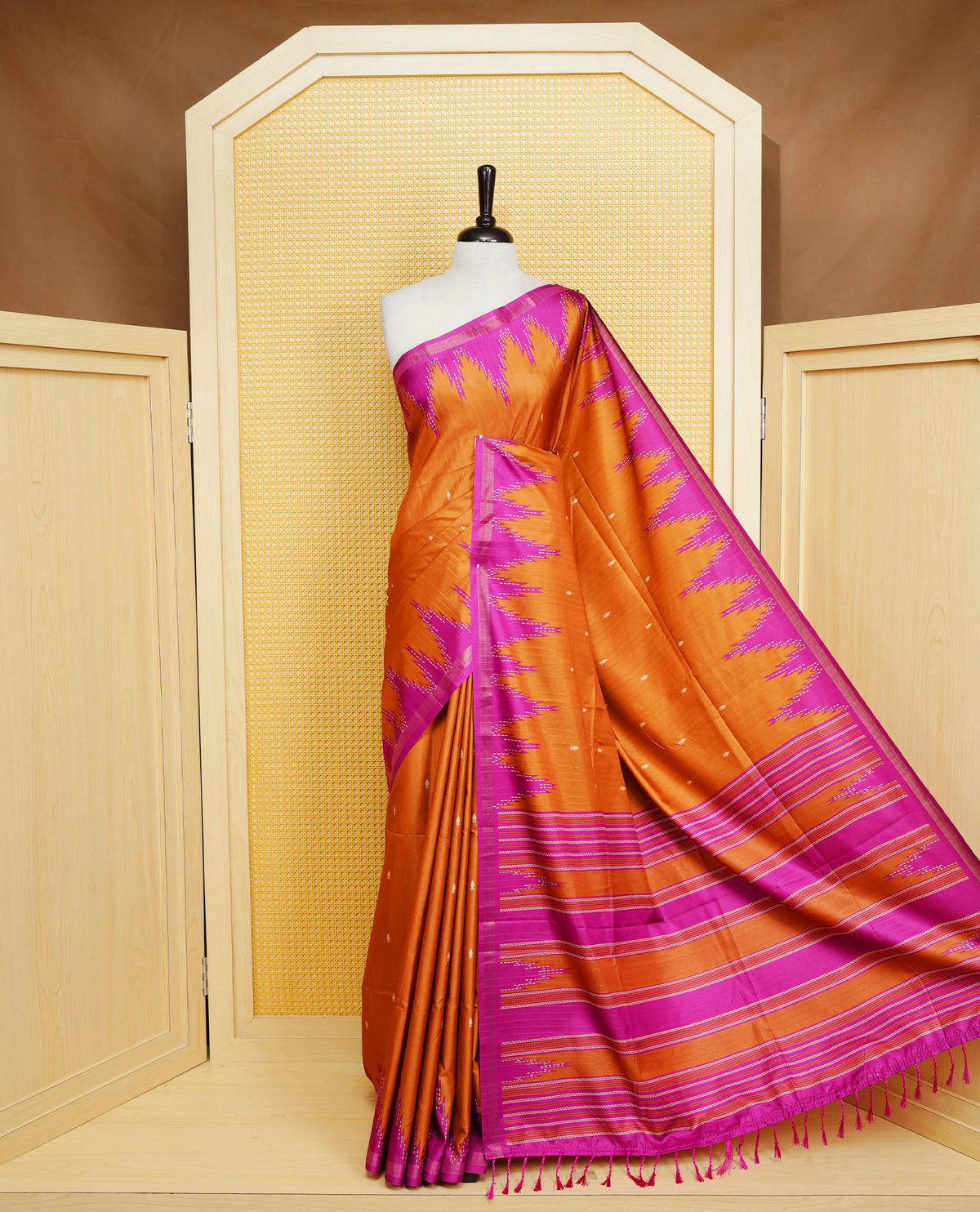 Rust orange and magenta  Colour Kattan silk saree featuring buttas all over the body, a temple-designed border &  a contrasting striped pallu with tassels. Paired with a matching contrast-striped blouse piece.