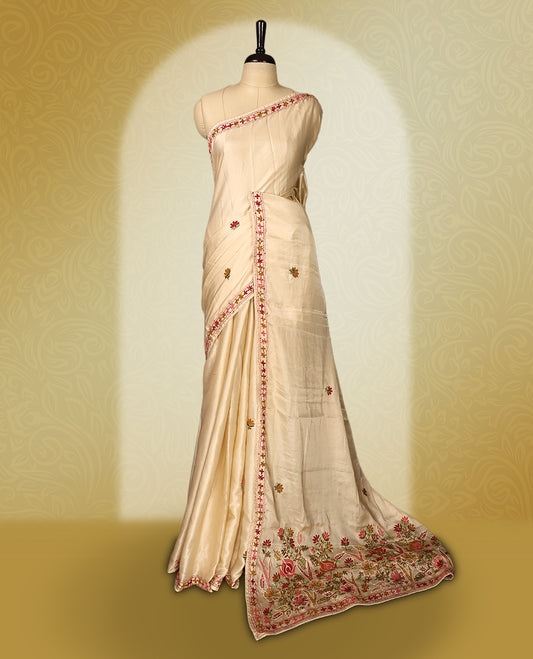 Cream colour pure tussar saree adorned with delicate pink and green floral embroidery along the border and scattered motifs across the body, paired with a matching blouse.