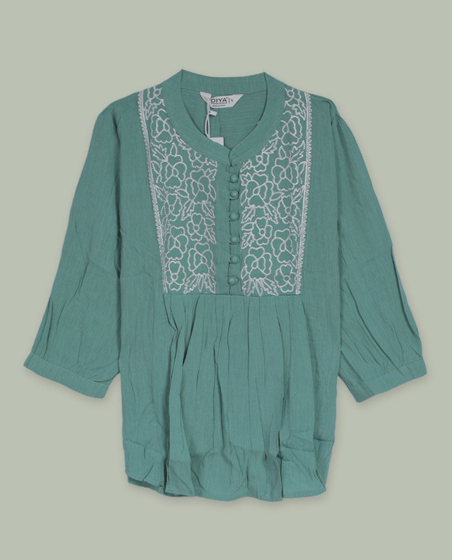 Sea green three-quarter sleeve tunic top with rounded band neckline, front floral embroidered yoke, fabric-covered button placket, and soft pleating below the yoke.