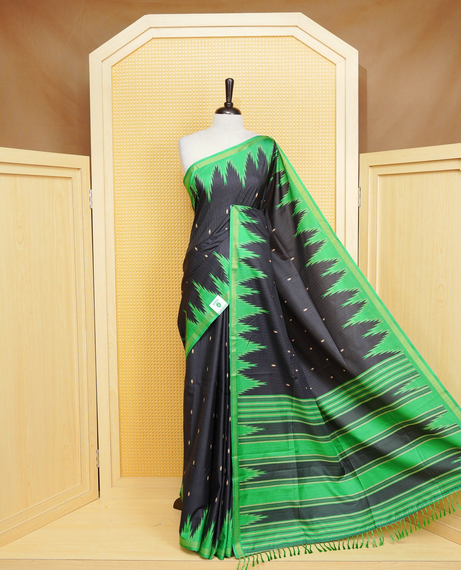 Black And Green Colour Kattan silk saree featuring buttas all over the body, a temple-designed border &  a contrasting striped pallu with tassels. Paired with a matching contrast-striped blouse piece.