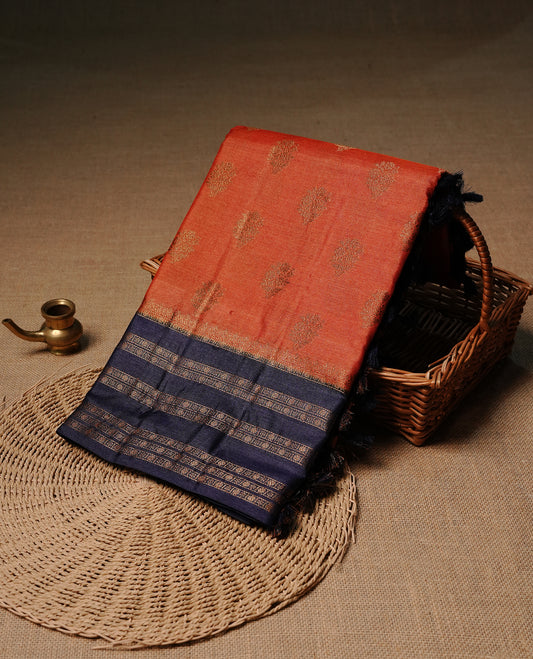 Rust orange colour pure tussar Banaras silk saree featuring elegant gold zari motifs across the body, complemented by a contrast Navy blue border with rich zari detailing. Comes with a matching blouse piece