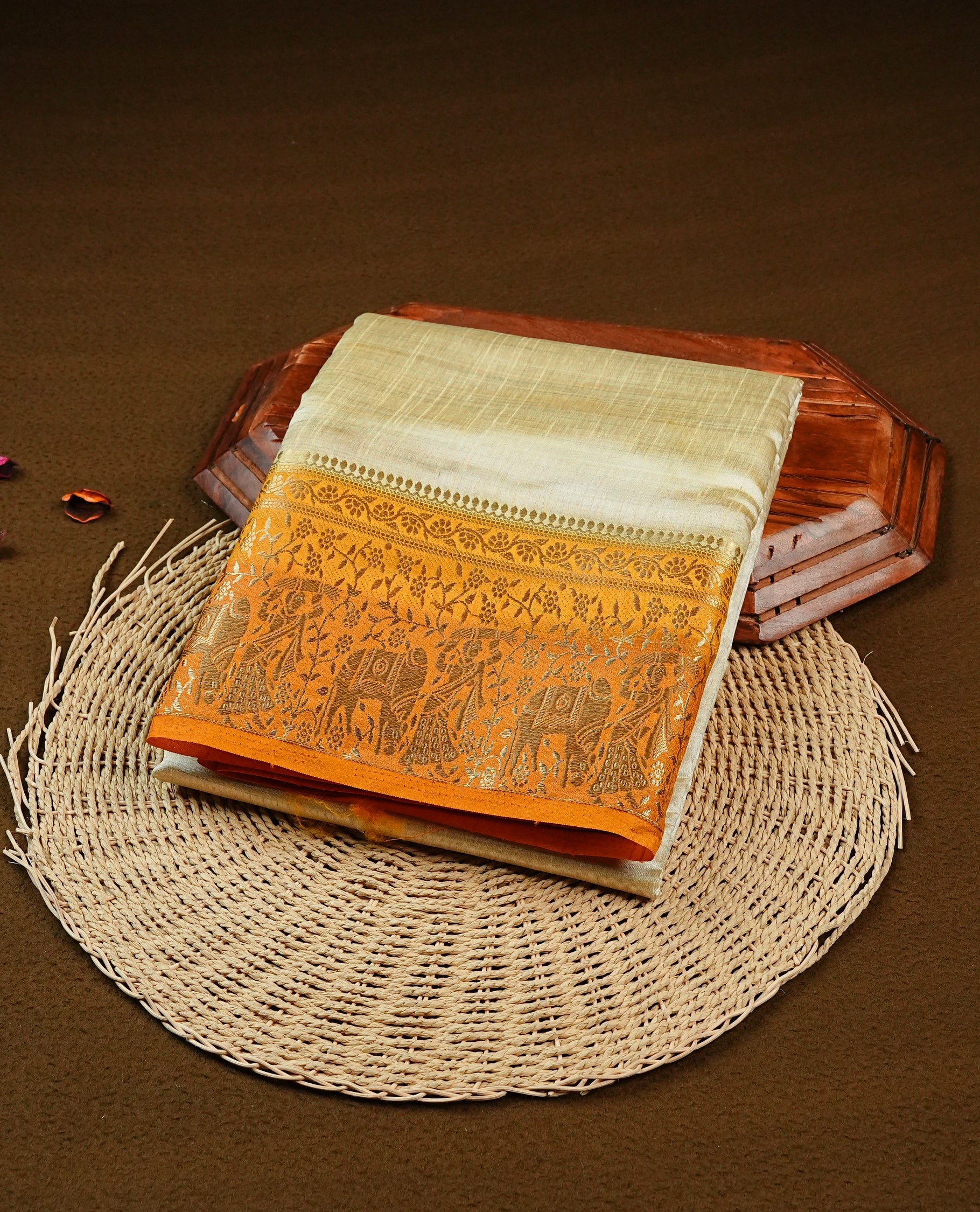 Light gold tussar saree featuring Elegant plain body, complemented by contrast Orange colour with Gold zari Floral kodi with Elephant Pattern border, comes with matching blouse piece.