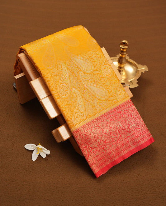 Mustard yellow colour semi silk brocade saree featuring intricate Gold Floral kodi & leaf patterns across the body, complemented by a contrast Red colour woven border and pallu, paired with a matching blouse.