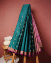 Teal colour soft silk saree featuring Gold zari  motifs on body, complemented by contrast Magenta colour with traditional border, paired with matching blouse piece.