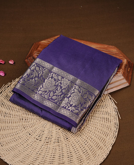 Indigo colour semi Tussar silk saree featuring an elegant plain body, complemented by a self colour border adorned with traditional gold zari floral kodi patterns. Comes paired with a matching blouse piece.