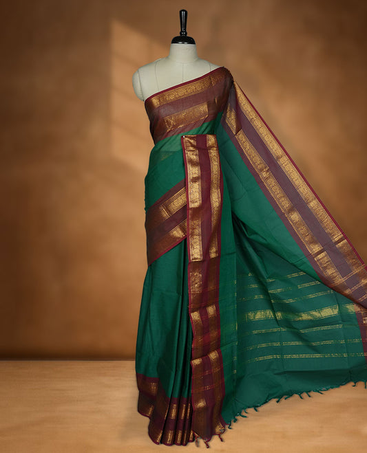 Dark green colour chettinad cotton saree featuring elegant plain body highlighting contrast maroon colour colour with gold zari traditional border, pallu and paired with matching blouse piece.