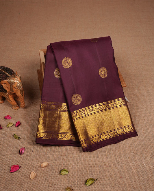 Dark chocolate colour pure traditional Kancheepuram silk saree adorned with elegant peacock and chakra motifs across the body, featuring rich gold zari traditional borders, beautifully paired with a matching blouse piece.