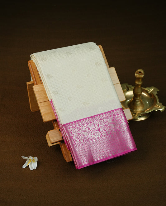 Cream colour semi wedding saree featuring light gold zari check with motifs on body complemented by contrast magenta colour with traditional border, comes with matching blouse piece.