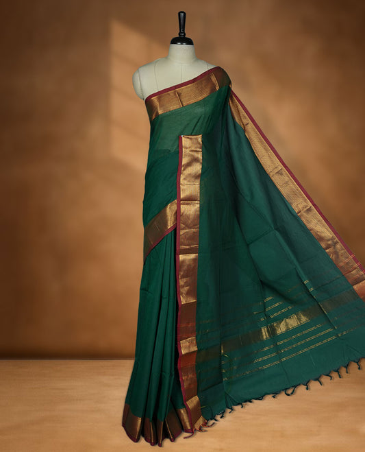 Dark green colour chettinad cotton saree featuring elegant plain body highlighting contrast maroon colour colour with gold zari traditional border, pallu and paired with matching blouse piece.