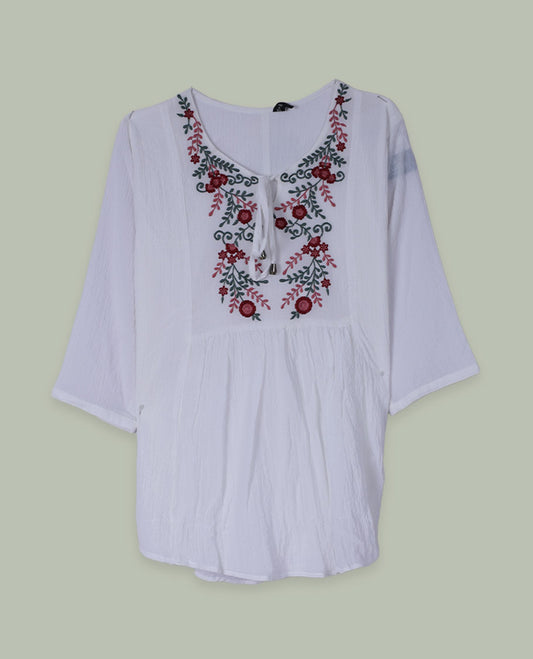 White three-quarter sleeve tunic top with round neckline and front yoke featuring red and green floral embroidery with tie-up detail at the neck.