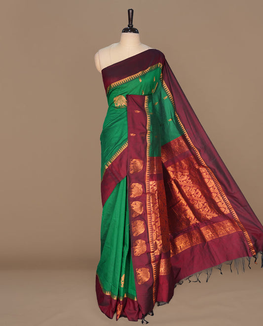 Green colour kalyani cotton saree featuring gold zari motifs on body, complemented by contrast maroon color with copper zari elephant pattern border , paired with matching blouse piece.