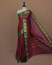 Maroon colour sungudi cotton saree featuring gold zari check pattern across body, contrast green colour with gold zari peacock and floral pattern on border, without blouse piece.