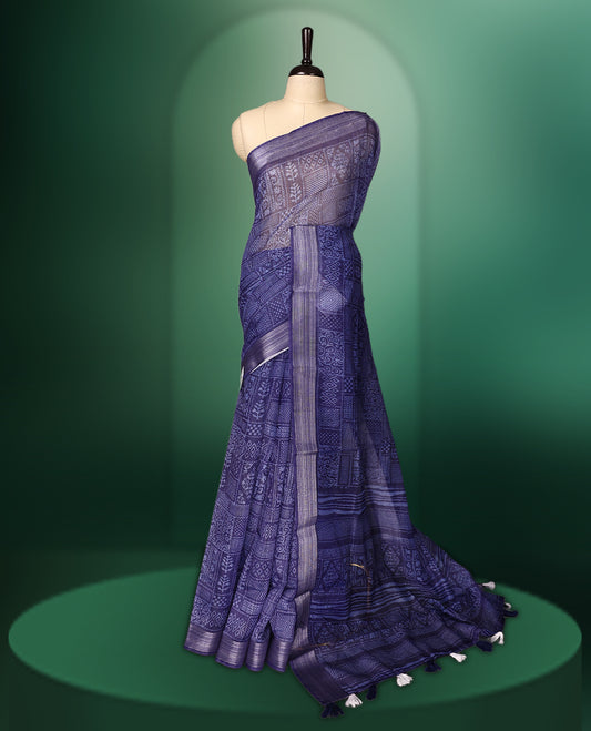 Blue colour saree featuring intricate woven geometric and floral patterns across the body and pallu, highlighted with a subtle striped border and tassels, paired with a matching blouse