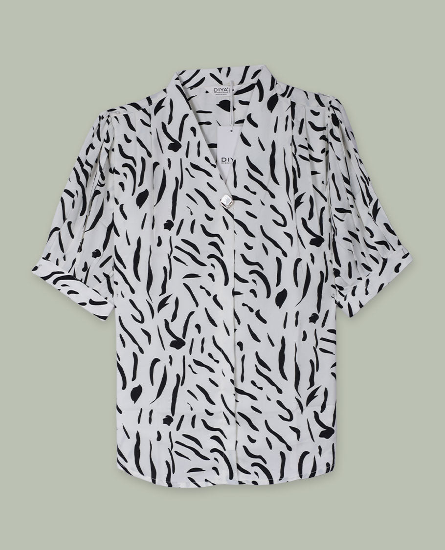 White and black abstract printed shirt top with notched lapel collar, single visible button at front, elbow-length sleeves, and softly gathered shoulders.