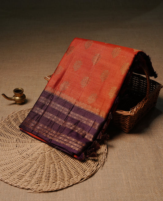 Rust orange colour pure tussar Banaras silk saree featuring elegant gold zari motifs across the body, complemented by a contrast Purple border with rich zari detailing. Comes with a matching blouse piece