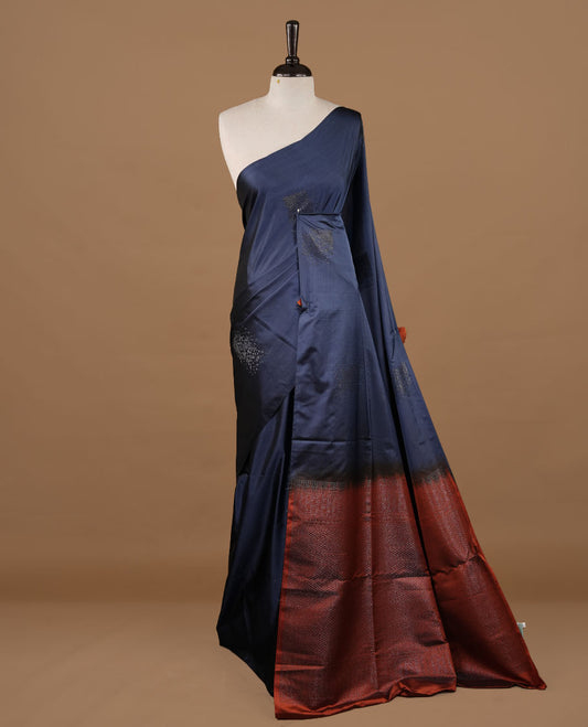 Navy blue colour soft silk saree features a sleek borderless design with intricate antique zari motifs, flowing into a striking contrast rust orange pallu and a matching blouse piece.