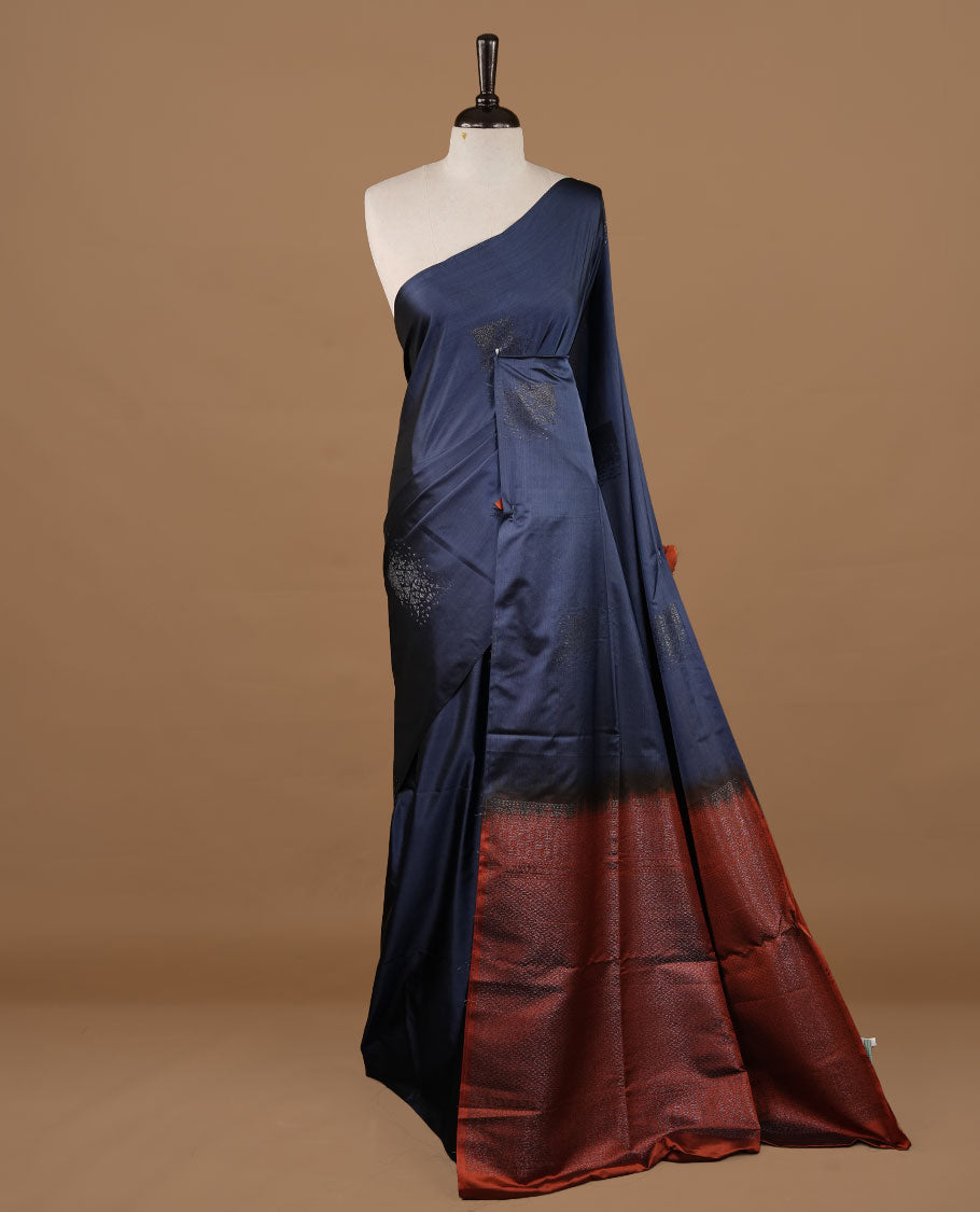 Navy blue colour soft silk saree features a sleek borderless design with intricate antique zari motifs, flowing into a striking contrast rust orange pallu and a matching blouse piece.