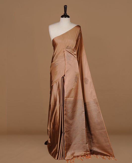 Dusty orange soft silk saree features a sleek borderless design with intricate antique zari motifs, flowing into a seamless self colored pallu and a matching blouse piece.