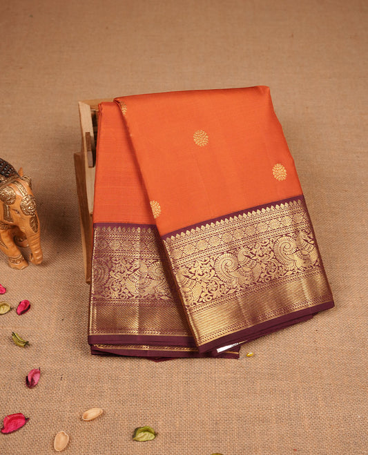 Rust orange colour pure traditional Kancheepuram silk saree adorned with gold zari motifs across the body, featuring elegant contrast Chocolate colour traditional borders, beautifully paired with a matching blouse piece.