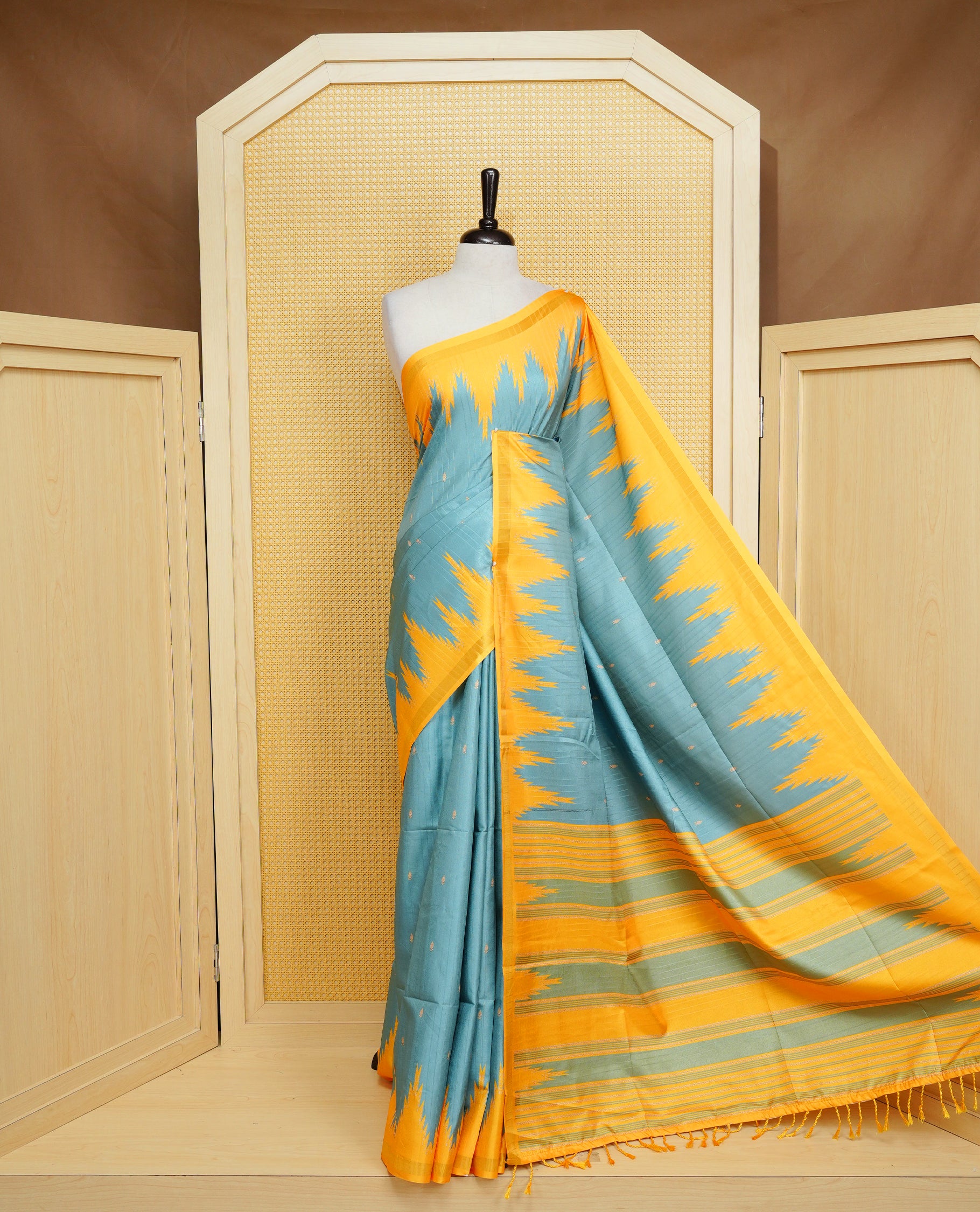 Teal Green And Yellow Colour Kattan silk saree featuring buttas all over the body, a temple-designed border &  a contrasting striped pallu with tassels. Paired with a matching contrast-striped blouse piece.