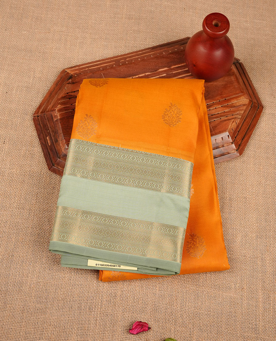 Dark mango yellow colour Vasundhara silk saree featuring elegant gold zari buttas across the body, complemented by a contrast pista green zari border, and paired with a matching blouse piece.