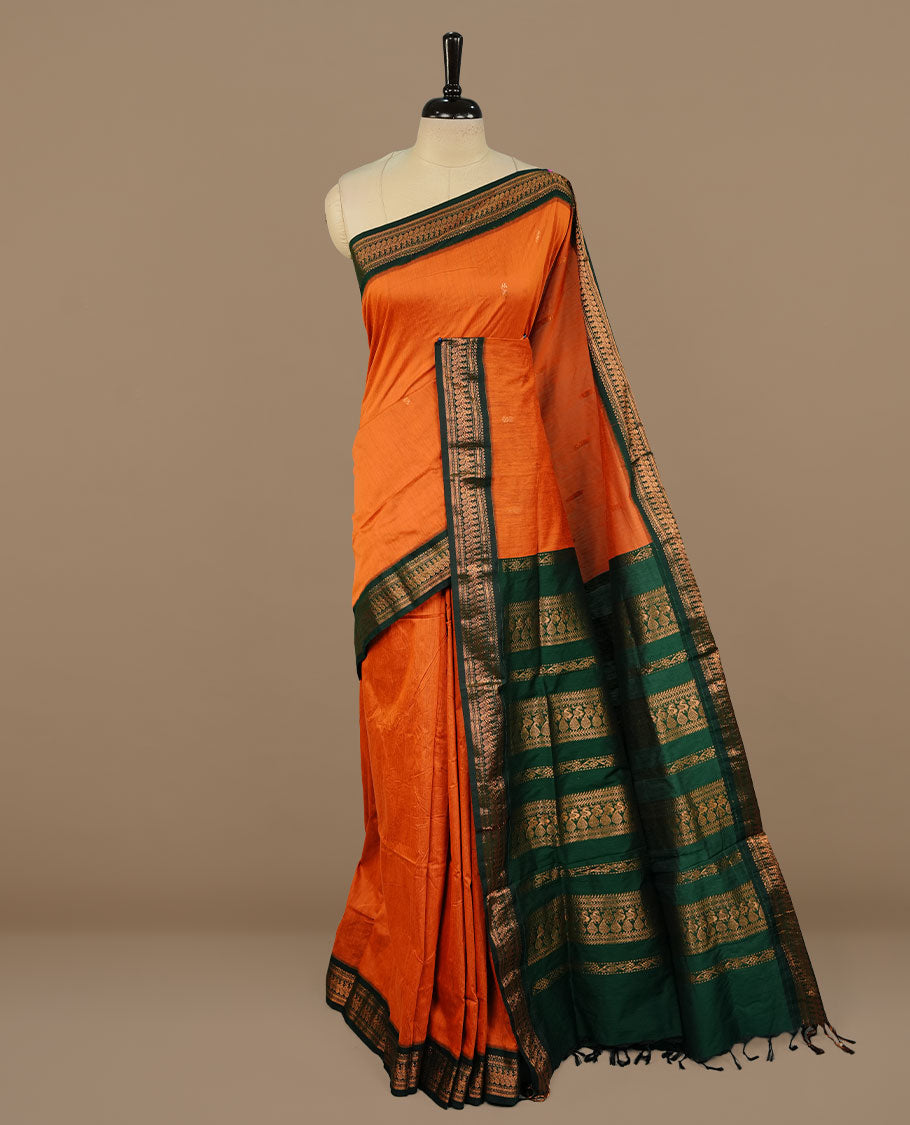 Rust orange colour kalyani cotton saree featuring gold zari motifs on body, complemented by green colour with zari border, paired with matching blouse piece.