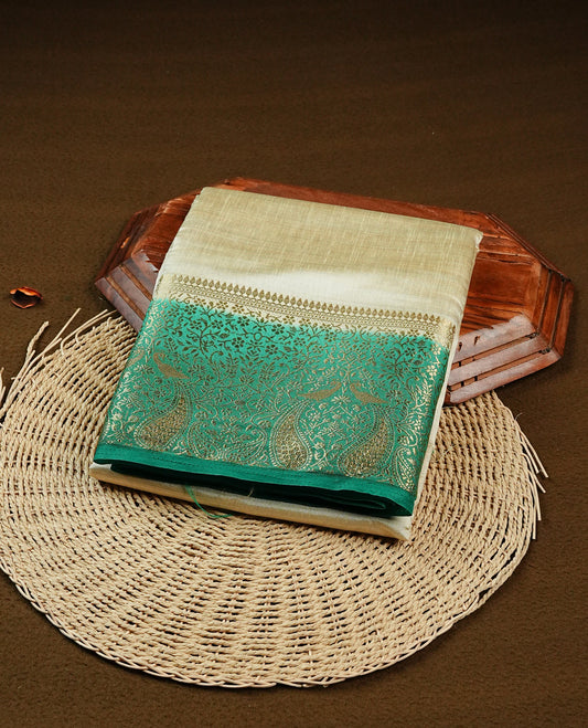 Light gold tussar saree featuring Elegant plain body, complemented by contrast green colour with Gold zari Floral kodi with Peacock Pattern border, comes with matching blouse piece.