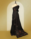 Black colour pure tussar saree adorned with delicate multicolour floral embroidery along the border and scattered motifs across the body, paired with a matching blouse.