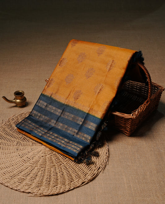 Mustard colour pure tussar banaras silk saree featuring gold zari motifs on body, highlighting contrast teal colour with zari border, paired with matching blouse piece.