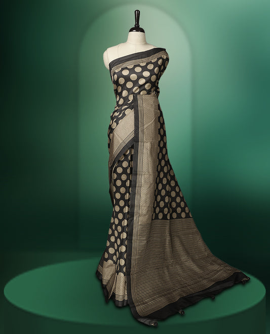 Charcoal Black colour saree featuring bold golden polka dot motifs all over the body, complemented by a sleek striped woven border and pallu, and paired with a matching blouse