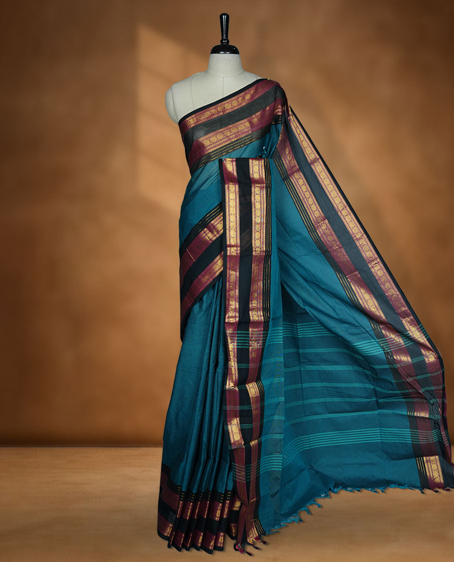 Teal colour chettinad cotton saree featuring plain body, contrast black and red colour with traditional gold zari border paired with matching blouse.