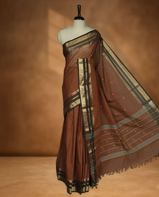 Brown colour chettinad cotton saree featuring small gold zari buttas on body highlighting contrast dark chocolate colour with gold zari traditional border, pallu and paired with matching blouse piece.