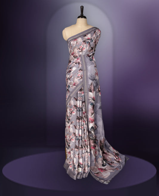 Grey colour  saree adorned with elegant floral prints on the body, enhanced with a subtle matching border, complemented by a beautifully printed pallu featuring blooming flowers, and paired with a matching blouse.