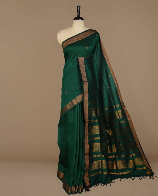 Dark green colour kalyani cotton saree featuring gold zari motifs on body, complemented by selfcolour with Antique zari border, paired with matching blouse piece.