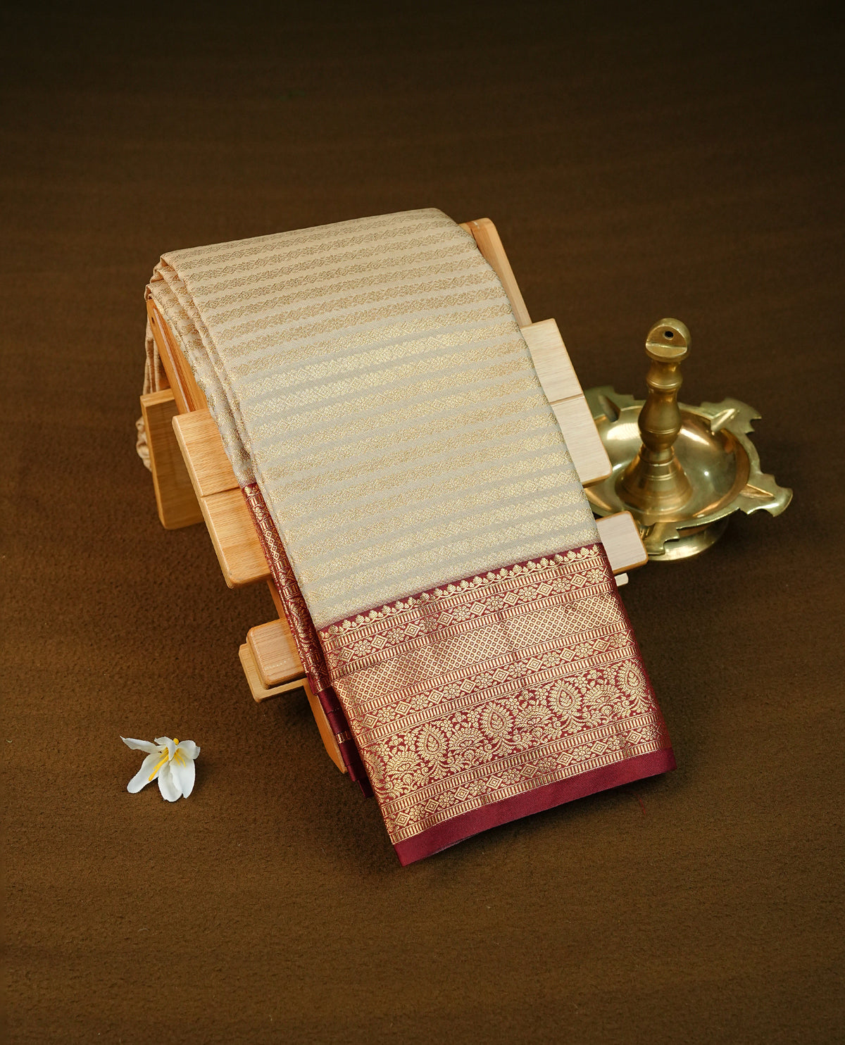 Beige colour semi wedding saree featuring gold zari stripes across the body, complemented by maroon colour with traditional border. Comes with a matching blouse piece.